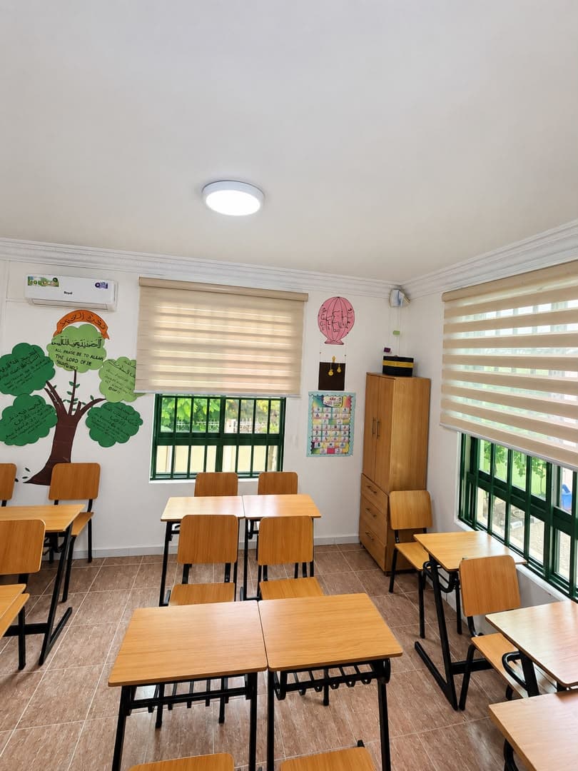 A classroom with wooden desks, green window frames and a paper tree on the wall.